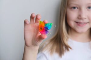 Smiling child holding a colorful orthodontic retainer during an early orthodontic visit.
